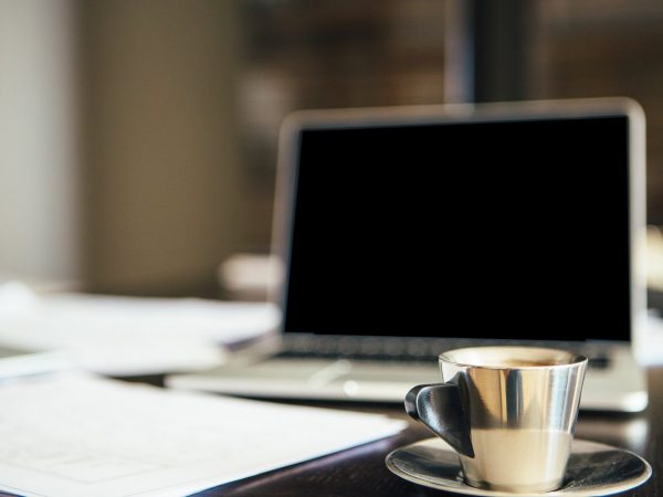 Close-up of silver cup of coffee on table against of laptop